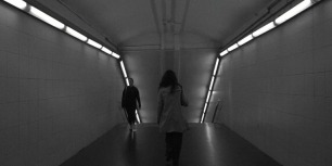 Una jove avança pels passadissos del metro de Barcelona, captada en blanc i negre, mentre la llum artificial dels fluorescents il·lumina el seu pas cap a les andanes.